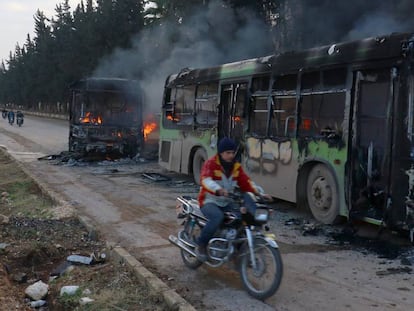 Un home passa amb moto pel costat d'un dels autobusos calcinats a Idlib quan es dirigien a evacuar els civilis de Fua i Kefraia.