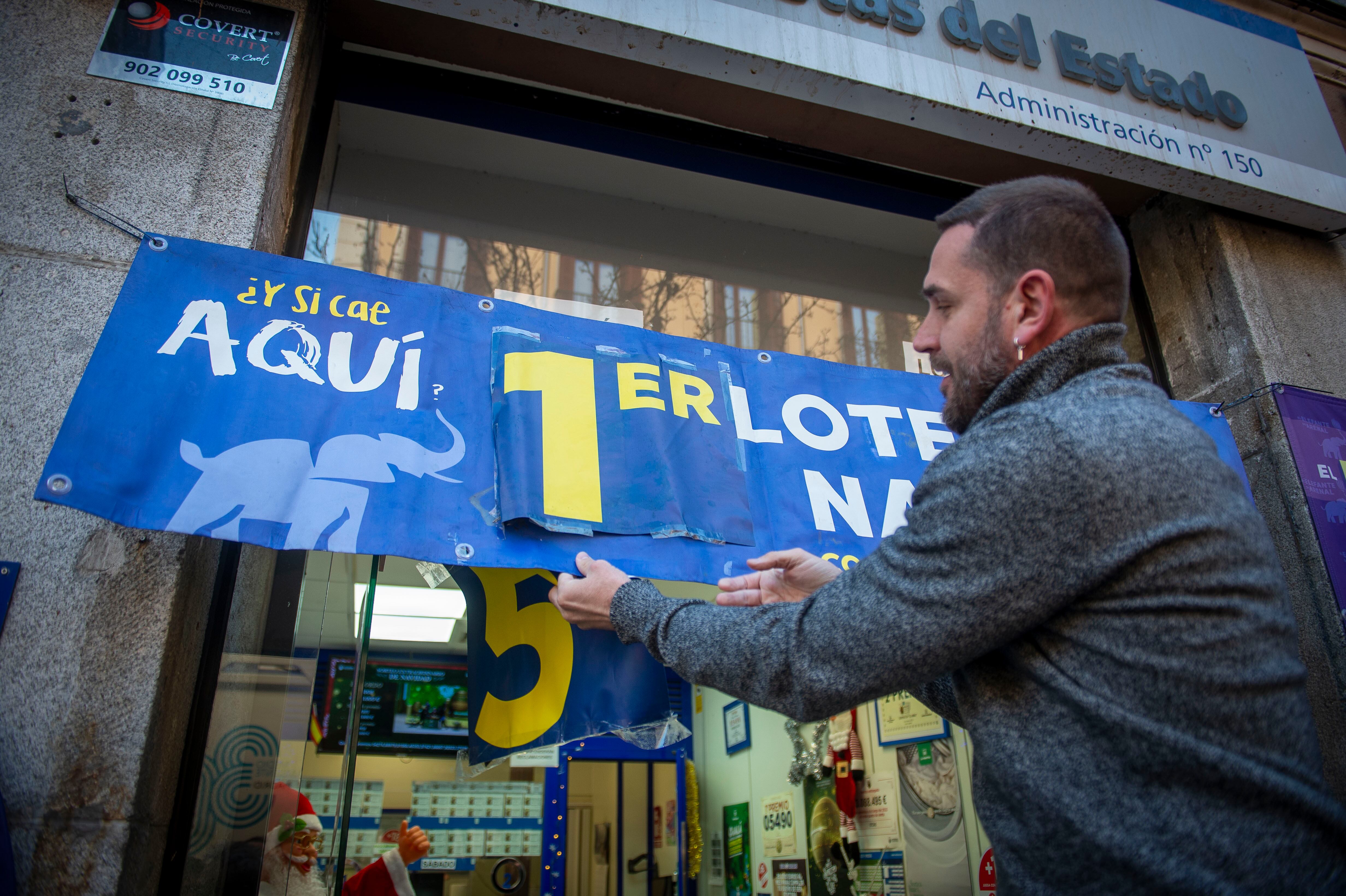Un funcionario de la administración loteria El Elefante del Arenal coloca el cartel del primer premio de la Lotería de Navidad. 