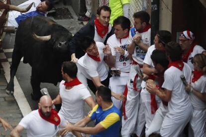 Uno de los toros de la ganadería de Fuente Ymbro tras un grupo de mozos a su paso por la calle de la Estafeta.