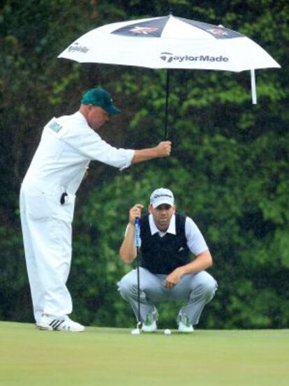 El caddie de Sergio García le protege de la lluvia en el hoyo 5.