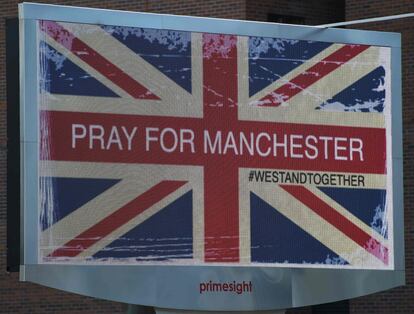 Painel eletrônico com a bandeira do Reino Unido e a frase "Rezem por Manchester" próximo à Arena Manchester