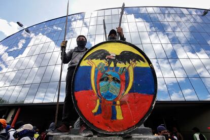 Indígenas de Ecuador se paran encima de un monumento portando un escudo con la bandera ecuatoriana, durante conversaciones entre líderes en la Casa de la Cultura Ecuatoriana. El presidente Guillermo Lasso permitió a unos cinco mil manifestantes entrar a la emblemática Casa de la Cultura, un lugar simbólico para los pueblos originarios que desde el 13 de junio estaba bajo control de la fuerza pública.