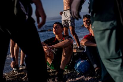 Un grupo de menores migrantes, sentados en la playa tras llegar a nado a Ceuta, espera en la arena rodeados de dos agentes de la Guardia Civil, el 19 de mayo.