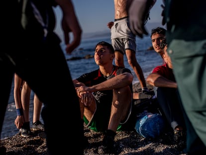 Un grupo de menores migrantes, sentados en la playa tras llegar a nado a Ceuta, espera en la arena rodeados de dos agentes de la Guardia Civil, el 19 de mayo.