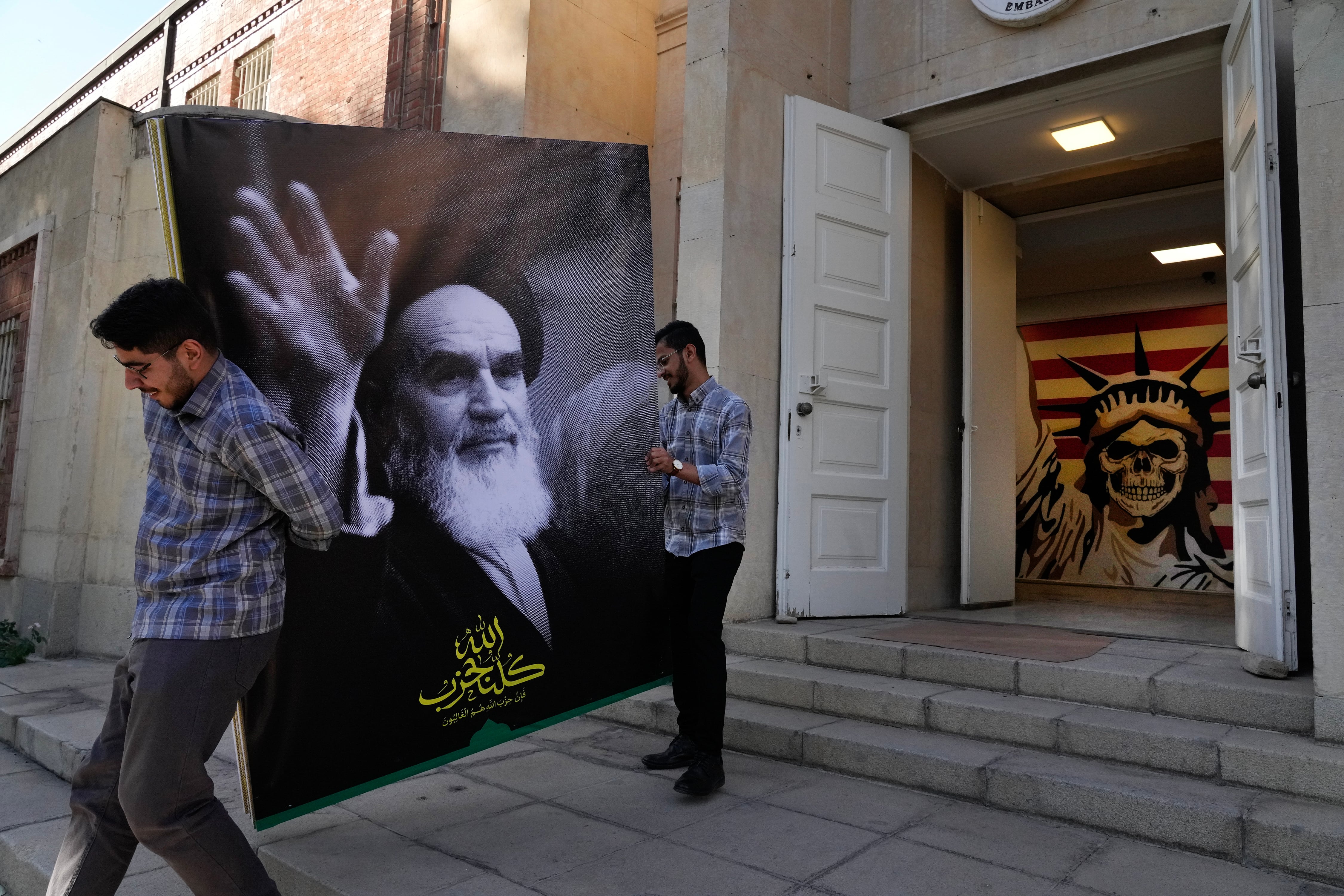 Two men carry a banner of the late Iranian revolutionary founder Ayatollah Khomeini at the entrance of the former U.S. Embassy, which has been turned into an anti-American museum, in Tehran, Iran, Tuesday, Oct. 22, 2024. (AP Photo/Vahid Salemi)    ----PIEFOTO----     Una pancarta del ayatolá Jomeini en la entrada de la antigua Embajada de EE UU de Teherán.