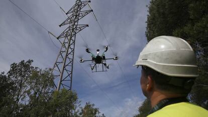 Un operario trabaja con un dron en una torre de alta tensión.