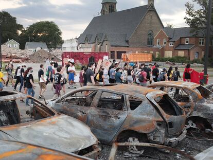 Um grupo de manifestantes pacíficos passa por carros queimados em Kenosha.