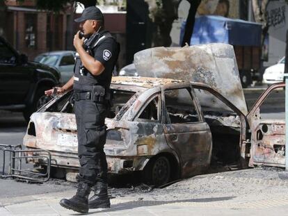 Um policial ao lado de um carro queimado por vândalos.