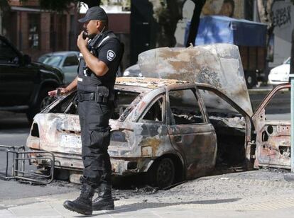 Um policial ao lado de um carro queimado por vândalos.