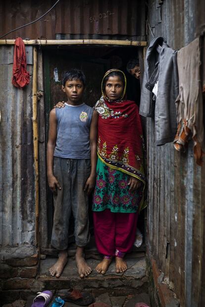 Emon posa en la puerta de su casa en uno de los slums de Dacca, capital de Bangladesh, junto a su madre, Shukhi Begum. La progenitora tiene 30 años y explica que el empleo inestable del padre del niño no da para pagar el alquiler. "Es ayudante de un transportista; unos días trabaja y otros no", dice. Ella no tiene empleo, pero asegura que, aunque lo tuviera, su hijo no podría dejar su labor como mecánico por la que gana 1.500 takas (unos 17 euros) al mes. "Sé que está prohibido. Sé que hago mal dejando que mis hijos trabajen, pero tengo que hacerlo para mantener a la familia", añade mientras observa a Emon cabizbajo.
