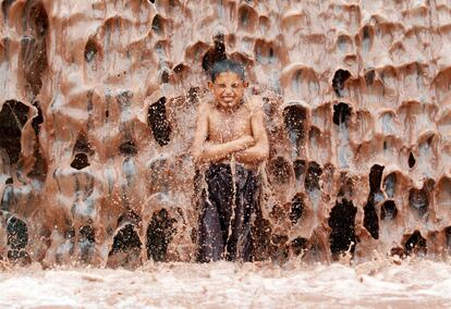 Un niño afgano se refresca bajo una cascada de barro a las afueras de la provincia de Jalalabad (Afganistán).