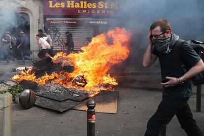 Um homem se protege ao passar por uma fogueira durante confrontos entre manifestantes e policiais no 1º de maio em Paris.