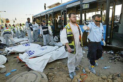 Policías y miembros de los servicios de socorro recuperan cadáveres tras la explosión de uno de los dos autobuses en Beersheva, al sur de Israel.