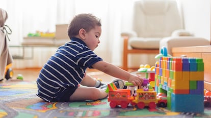 Un niño de dos años sentado en una alfombra y jugando con bloques de construcción.