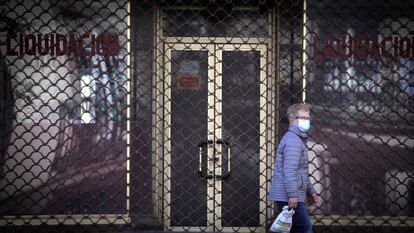 Una mujer ataviada con una mascarilla pasea junto a un negocio cerrado en A Coruña durante mayo de 2020.