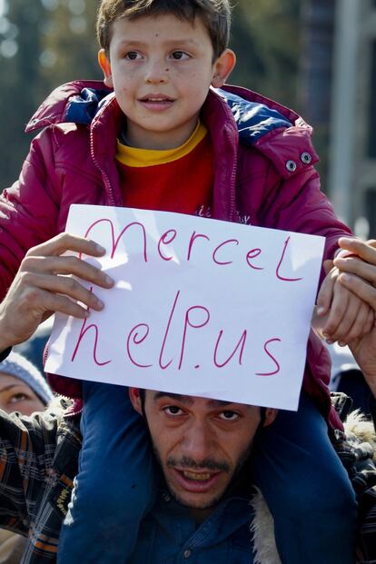 Un migrante con su hijo a hombros con un cartel pidiendo ayuda a Merkel en la frontera de Grecia con Macedonia, en el paso fronterizo de Idomeni.