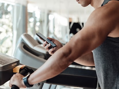 Una persona mira su teléfono móvil mientras utiliza una cinta de correr.