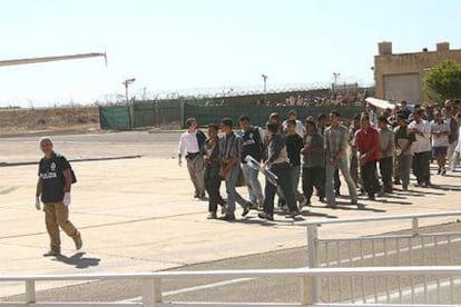 Un policía italiano guía a un grupo de inmigrantes hacia un avión que se dirigía a Libia desde la isla de Lampedusa el pasado domingo.