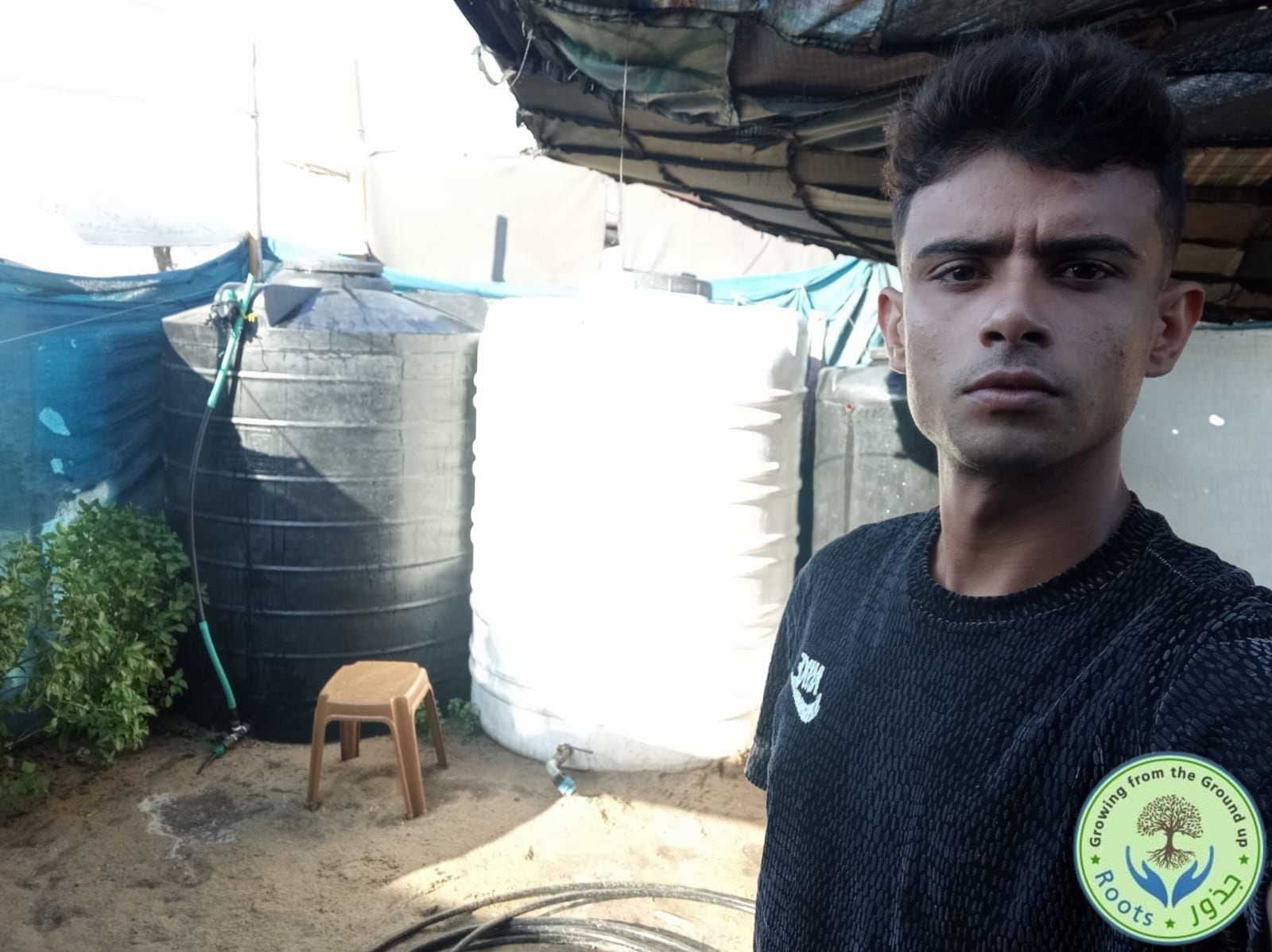 Abdallah Aljazzar, en el campo de desplazados de Al Mawasi, en el sur de la Franja de Gaza, al lado de los tanques gracias a los cuales se distribuye agua a decenas de familias sin que tengan necesidad de desplazarse. Fotografía cedida por Aljazzar.