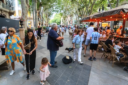 Un músico callejero toca para varios turistas en terrazas en el paseo del Born de Palma de Mallorca.