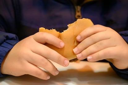 Detalle de las manos de un niño pequeño comiendo una hamburguesa.