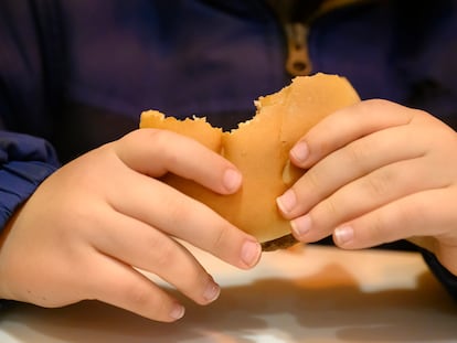 Detalle de las manos de un niño pequeño comiendo una hamburguesa.