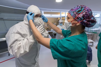 Una enfermera de la unidad de cuidados intensivos (UCI), ayuda a un compañero a colocarse las protecciones, en el hospital universitario Morales Meseguer de Murcia, el sábado 25 de abril.