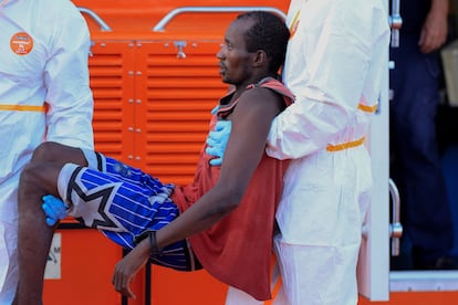 Dos sanitarios ayudan a desembarcar a uno de los migrantes del cayuco, el domingo.