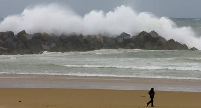 Un hombre se protege contra el viento y la lluvia en la playa de la Zurriola de San Sebastián.