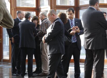 El rector Pérez camina con gesto pensativo por el Aula Magna dos días antes de las elecciones, rodeado por miembros de su equipo.