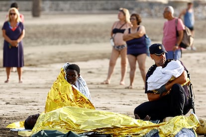 Un policía sujeta a un bebé mientras atiende a un grupo de migrantes que han llegado en un cayuco este viernes a la playa de Las Burras, en Gran Canaria. 
