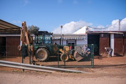 Vecinos de las viviendas inundadas frente al río Gévora en las casas aisladas de Gévora retiran el barro acumulado en la fachada con ayuda de un tractor.