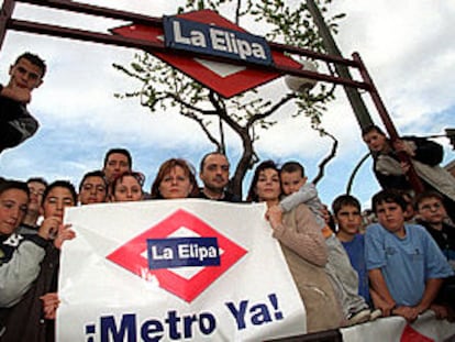 Un grupo de vecinos de La Elipa, debajo de una falsa entrada, muestra una pancarta en la que piden una línea de metro para su barrio.