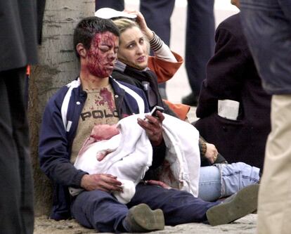 Dos personas heridas en la explosión de uno de los trenes en Atocha esperan en el suelo a ser atendidas.