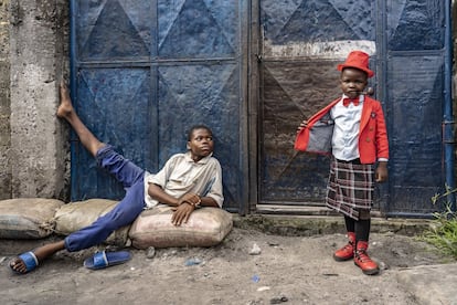 Israell Mbona (derecha), estudiante de cinco años y <em>sapeur</em> desde que tenía solo dos, posa en Kinshasa en 2019. Viste chaqueta de Big Guy, falda escocesa de Escocia, camisa de Unique, gorro que consiguió para Navidad, pipa de fabricación local y zapatos de Versace.