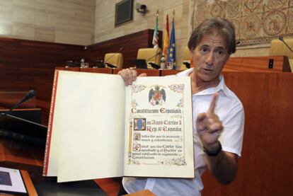 Pedro Escobar, líder de IU en Extremadura, muestra un ejemplar de la Constitución sobre el que juran o prometen los diputados regionales y que mantiene el escudo preconstitucional.