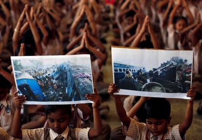 Niños sujetan imágenes del accidente de tren que tuvo lugar el pasado domingo en Pukhrayan, mientras rezan por las víctimas, en una escuela de Ahmedabad (India).