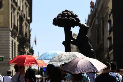 Los viandantes se protegen del sol con paraguas en la madrileña plaza del Sol, al lado del monumento del oso y el madroño.