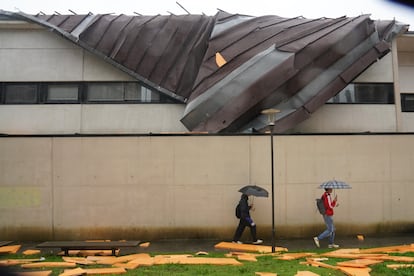 Dos personas caminan junto a los restos del tejado del Conservatorio de Música en Santiago de Compostela desprendido tras el fuerte viento, este miércoles. 