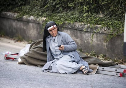 Una monja comprueba su teléfono móvil desde el suelo, junto a una escalera, tras el terremoto de Amatrice.