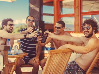 Cuatro hombres cisheterosexuales brindan con cerveza en un chiringuito
