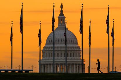 An early morning pedestrian is silhouetted against sunrise as he walks through the American flags on the National Mall with the U..S Capitol Building