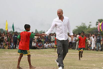 Zinedine Zidane estrecha la mano de su jovencísimo compañero de equipo durante un partido amistoso organizado en su honor en Mojlishpur, Gazipur, a 35 kilómetros de la capital Dacca.