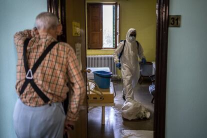 Un hombre espera en el exterior de su habitación en una residencia de mayores mientras los bomberos trabajan en la desinfección.