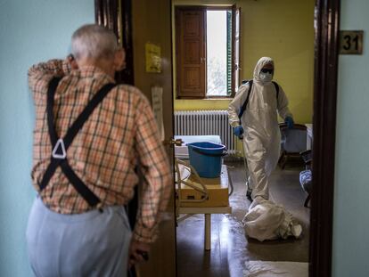 Un hombre espera en el exterior de su habitación en una residencia de mayores mientras los bomberos trabajan en la desinfección.