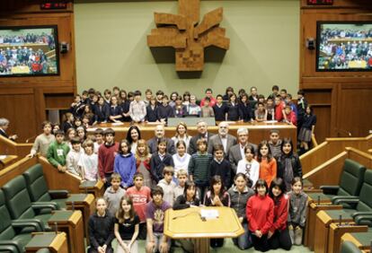 Los 75 escolares que participaron en la iniciativa posan en el salón de plenos del Parlamento junto a su presidenta, Arantza Quiroga (en la parte inferior de la sala, en el centro), y el resto de miembros de la Mesa de la Cámara.