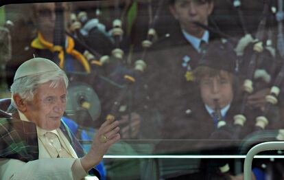 Benedicto XVI, con una bufanda escocesa, saluda desde el <i>papamóvil</i> a un grupo de gaiteros en las calles de Edimburgo.