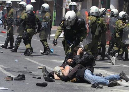 Un policía antidisturbios detiene a dos participantes en una manifestación cuando se dirigían al Parlamento griego.