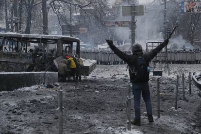 Un manifestante gesticula a la policía mientras otros se escudan tras un vehículo quemado durante los duros enfrentamientos que comenzaron el 19 de enero en Ucrania.