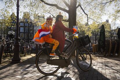 Una madre y su hija, que muestra un pulgar hacia arriba, ondea la bandera holandesa y viste de naranja con motivo de la celebración del Día del Rey en Países Bajos, recorren en bicicleta el canal Prinsengracht, en el centro de Ámsterdam.